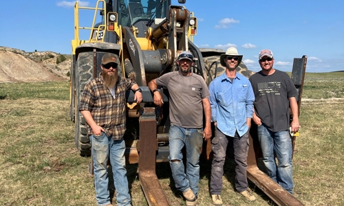 Dr. Tyler Lyson with his brother Derek Lyson and equipment operations team standing in front of a 60,000-pound front loader to transport the jacket to the highway.