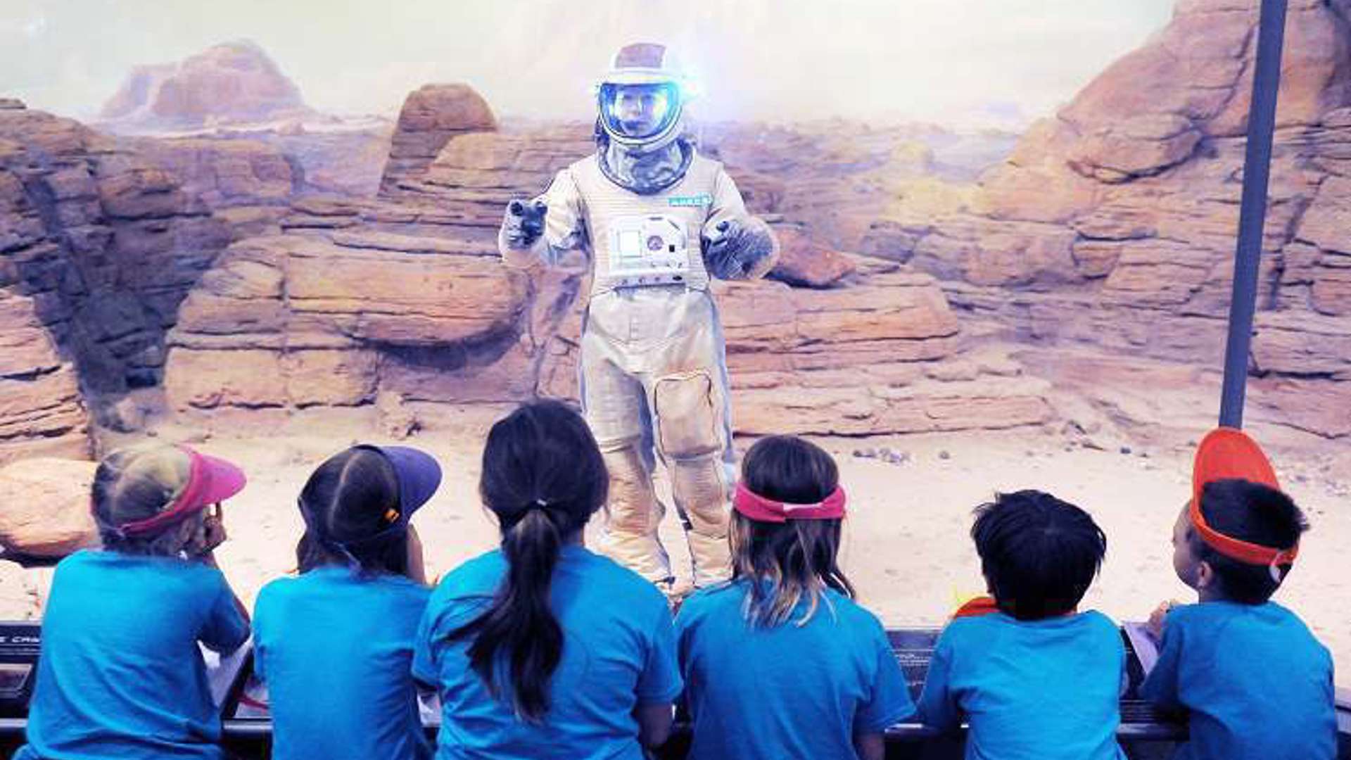 A person dressed in a space suit communicates with children, fostering curiosity about space and encouraging their interest in science.