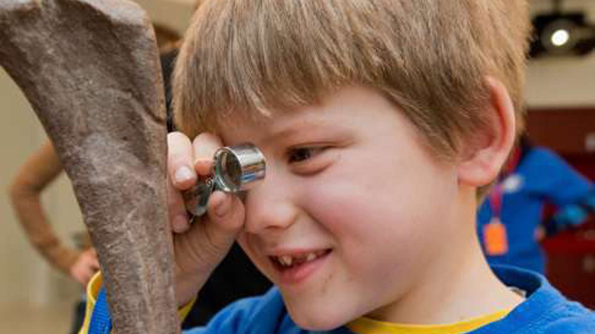 Child with short hair using a hand lens to look at the details in a fossilized bone