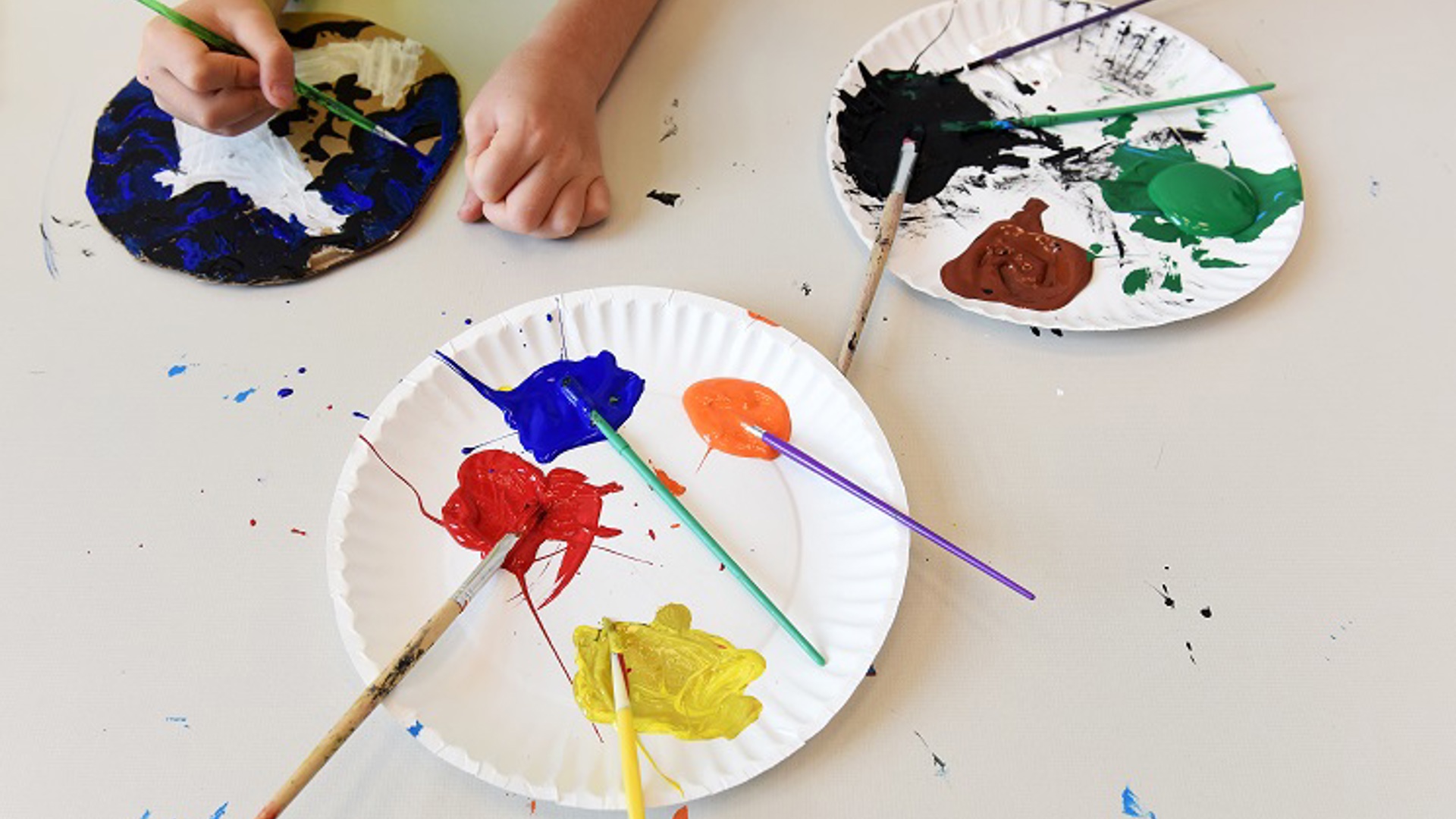 Paper plates with paint and brushes, with children's hands 