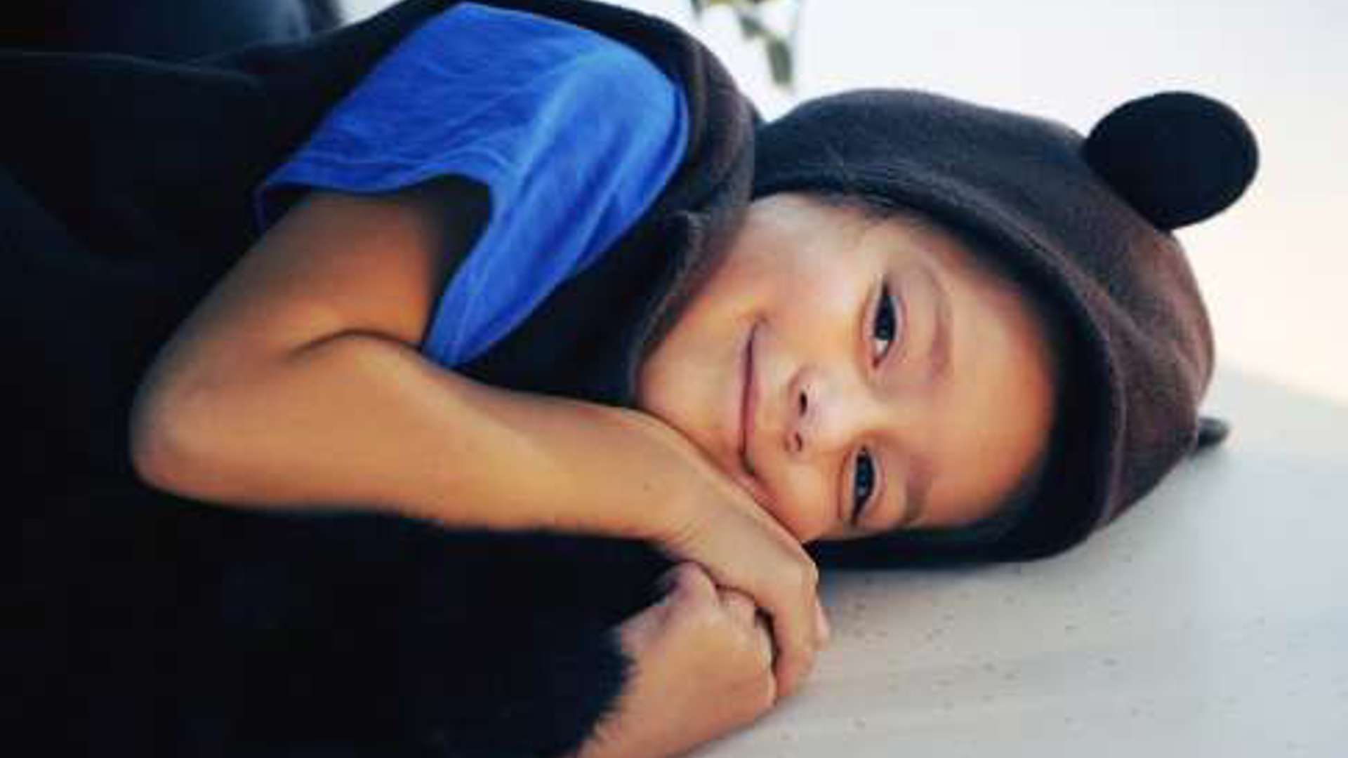 Young child laying on the floor, wearing a black bear costume
